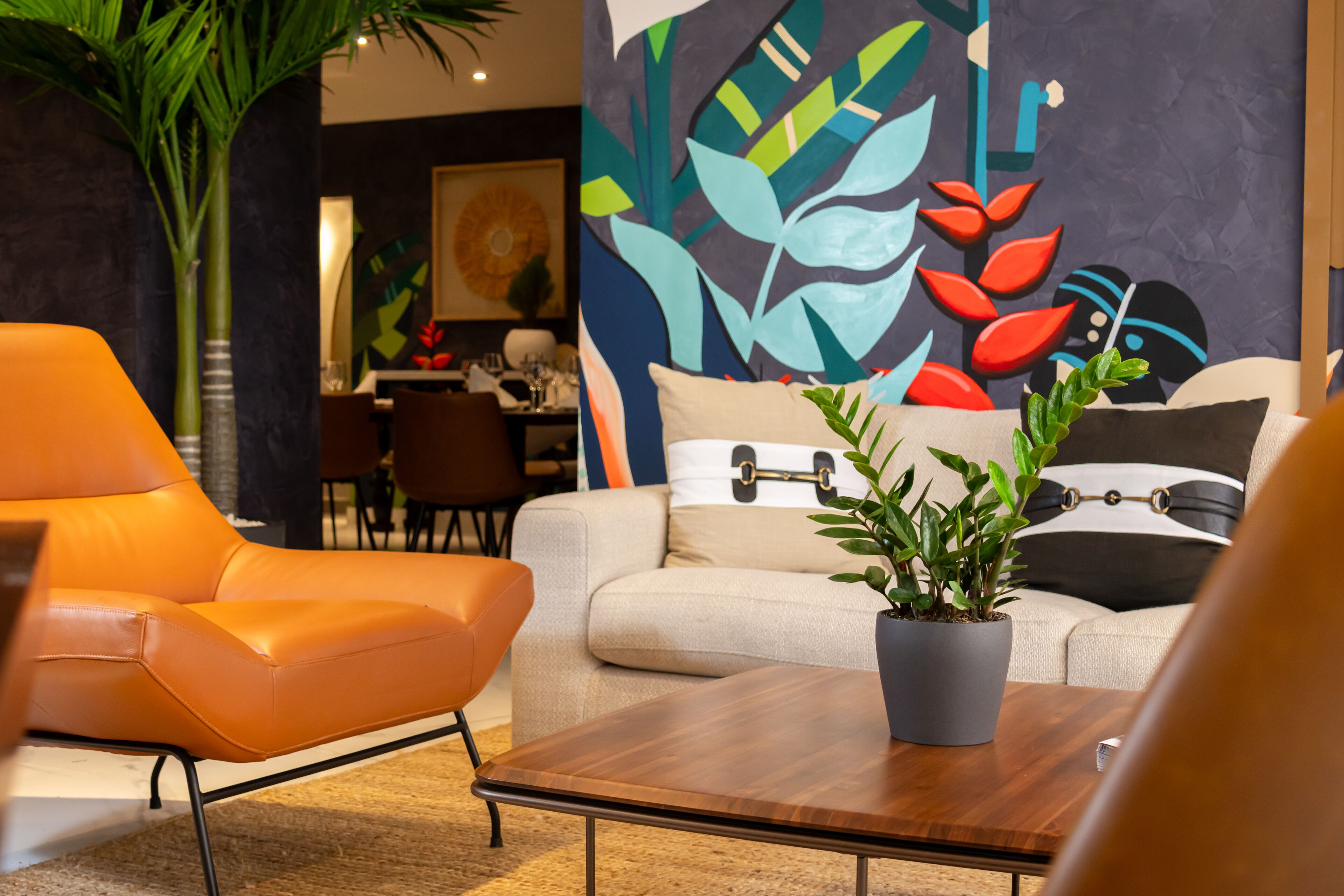 A modern living room with a sofa, an orange armchair, a wooden coffee table, and a potted plant.