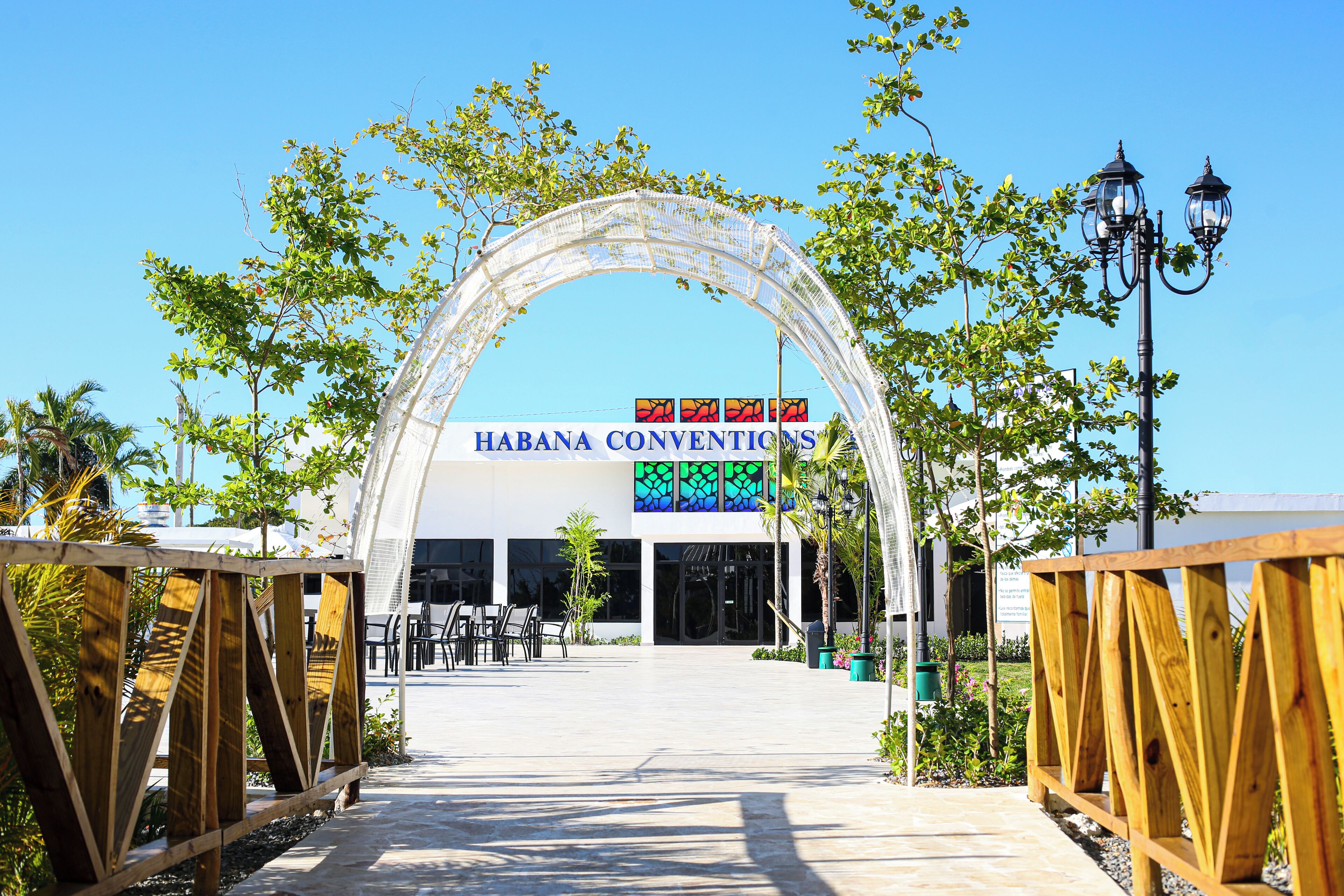 An entrance to the Habana Conventions building with a clear sky, a wooden archway, and a signboard.