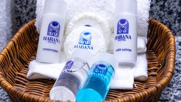 Un panier en osier contenant trois flacons de lotion pour le corps de la marque Habana Hotel, un flacon d’après-shampoing et un flacon bleu, le tout posé sur une serviette blanche.