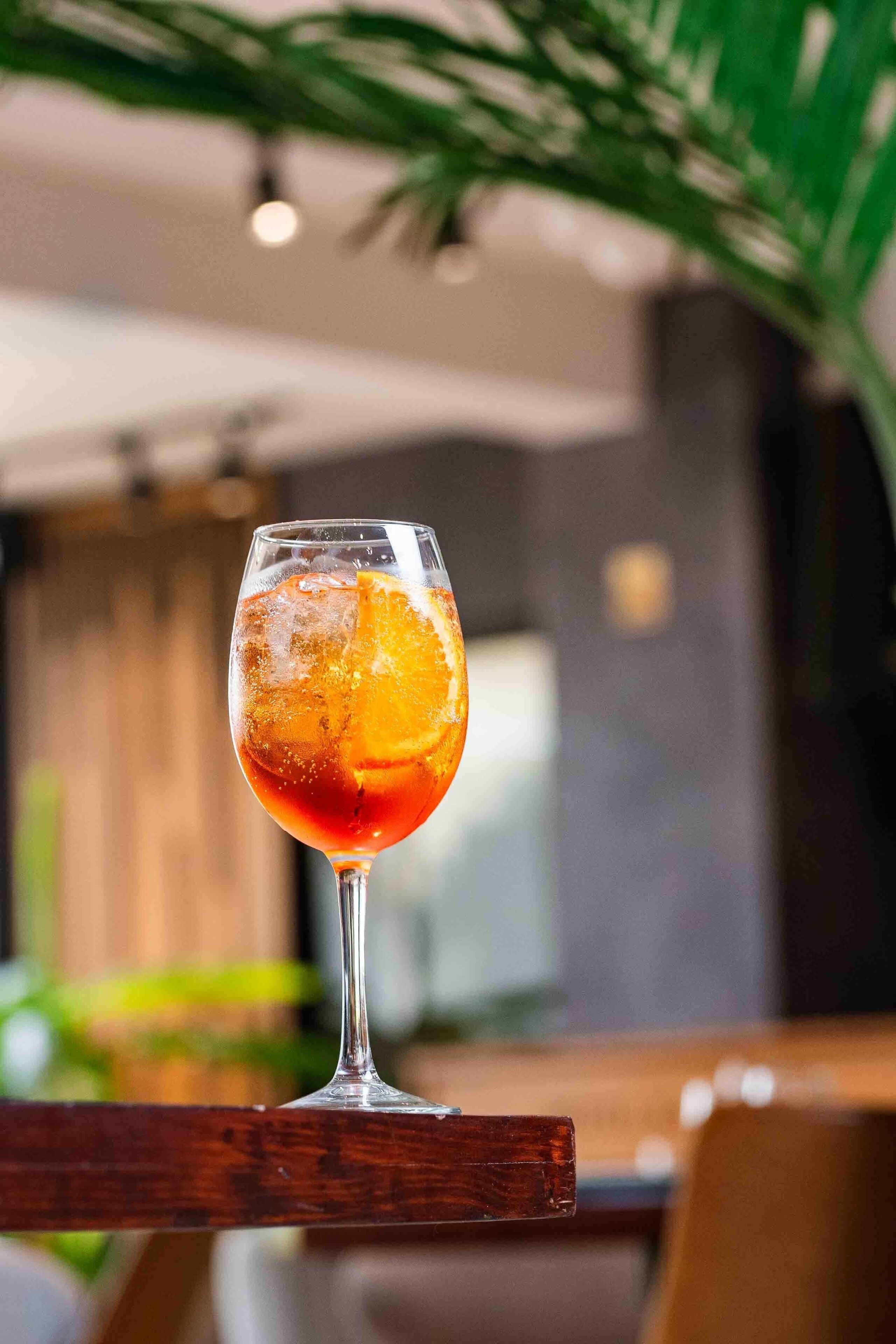 A glass of red beverage with an orange slice, placed on a wooden surface.