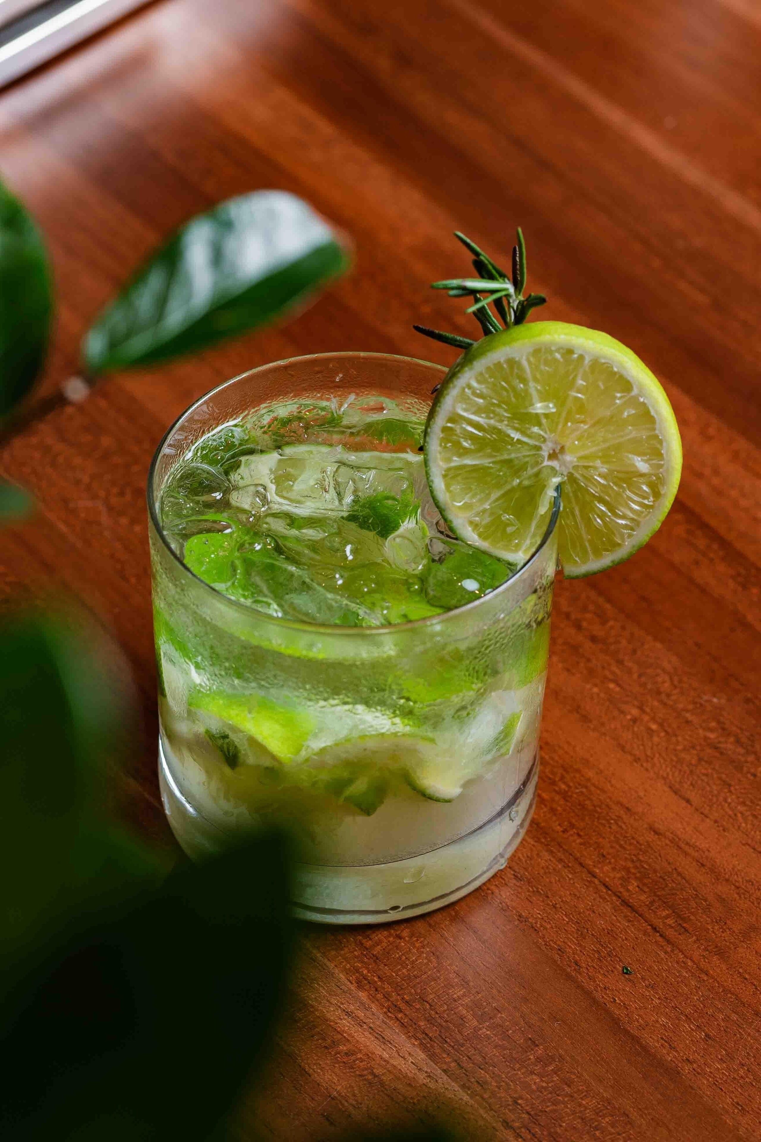 A glass of drink with lime and mint on a wooden table.