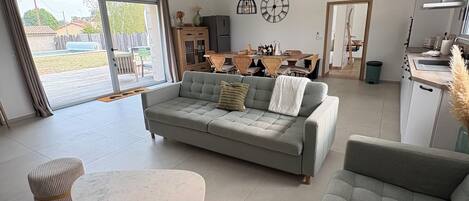 A modern living room with a sofa, a round table, and a dining area with chairs.