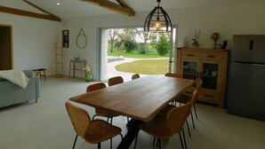 A spacious kitchen with a wooden dining table and chairs, a built-in refrigerator, and a view of the garden through a glass door. - Charming cottage with swimming pool in the heart of the Monbazillac vineyard (Monbazillac)
