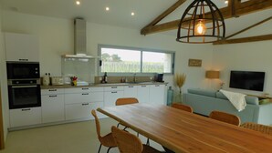 A modern kitchen with white cabinets, a wooden dining table, wicker chairs, and a large window. - Charming cottage with swimming pool in the heart of the Monbazillac vineyard (Monbazillac)