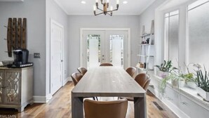 Un comedor con una larga mesa de madera, varias sillas, una lámpara de araña y vistas a una puerta que da a otra habitación.