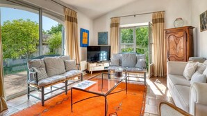 A spacious living room with a glass coffee table, two sofas, a TV, and large windows offering a view of greenery outside. - Peaceful villa (Tourrettes-sur-Loup)