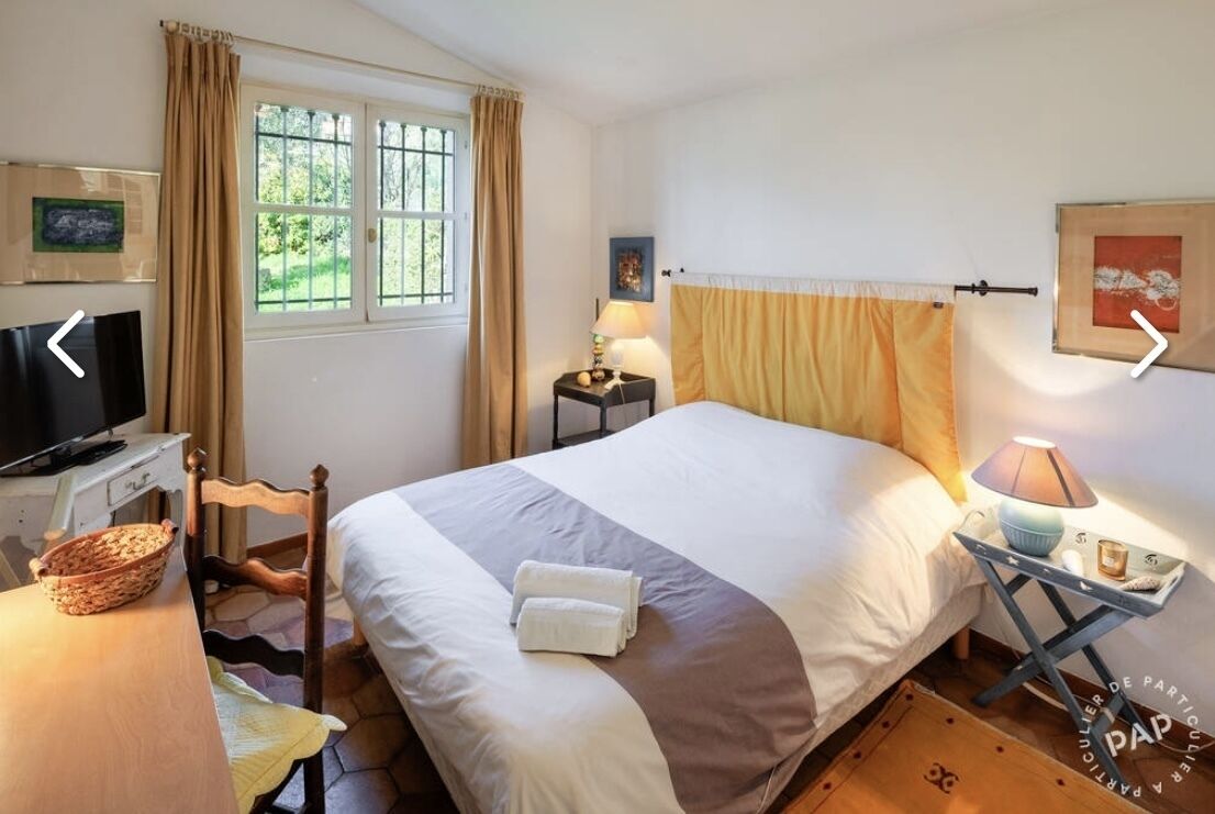 Un dormitorio con una cama, un escritorio con televisor, una lámpara y una ventana con cortinas.