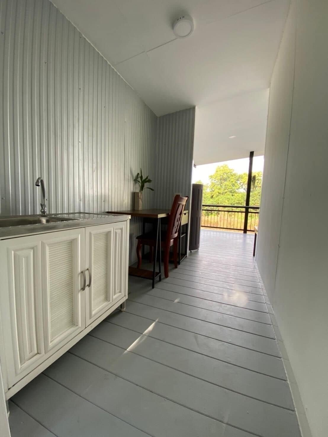 A balcony with a wooden floor, a white cabinet with a sink, and a dining table with chairs.