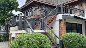 Una casa a due piani con un balcone, una scala e un giardino curato.