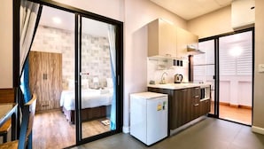 Una camera d'albergo moderna con un letto, un angolo cottura e una porta scorrevole che dà su un balcone.