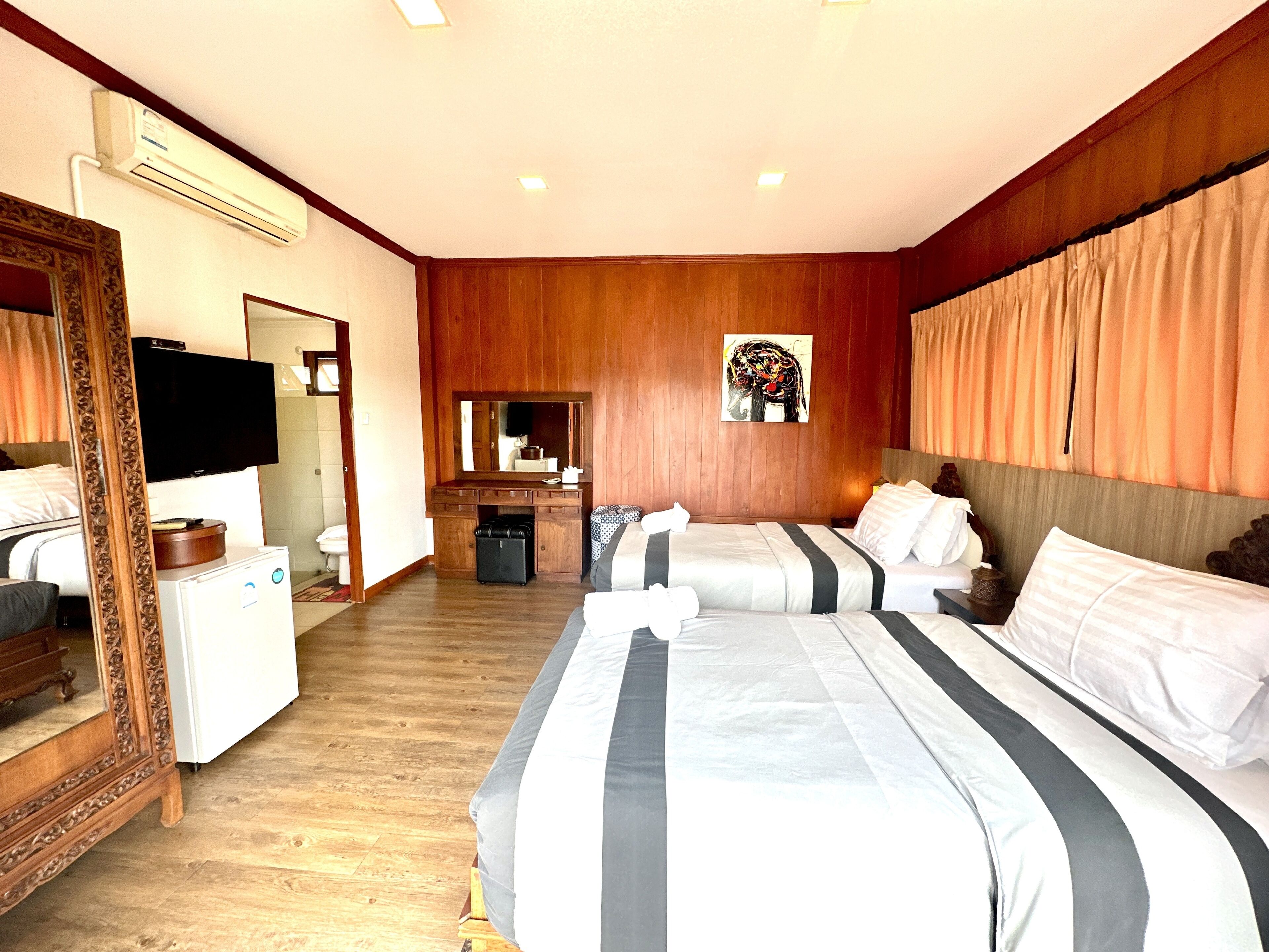 A hotel room with a large bed, a dresser, a mirror, a television, and an air conditioning unit.