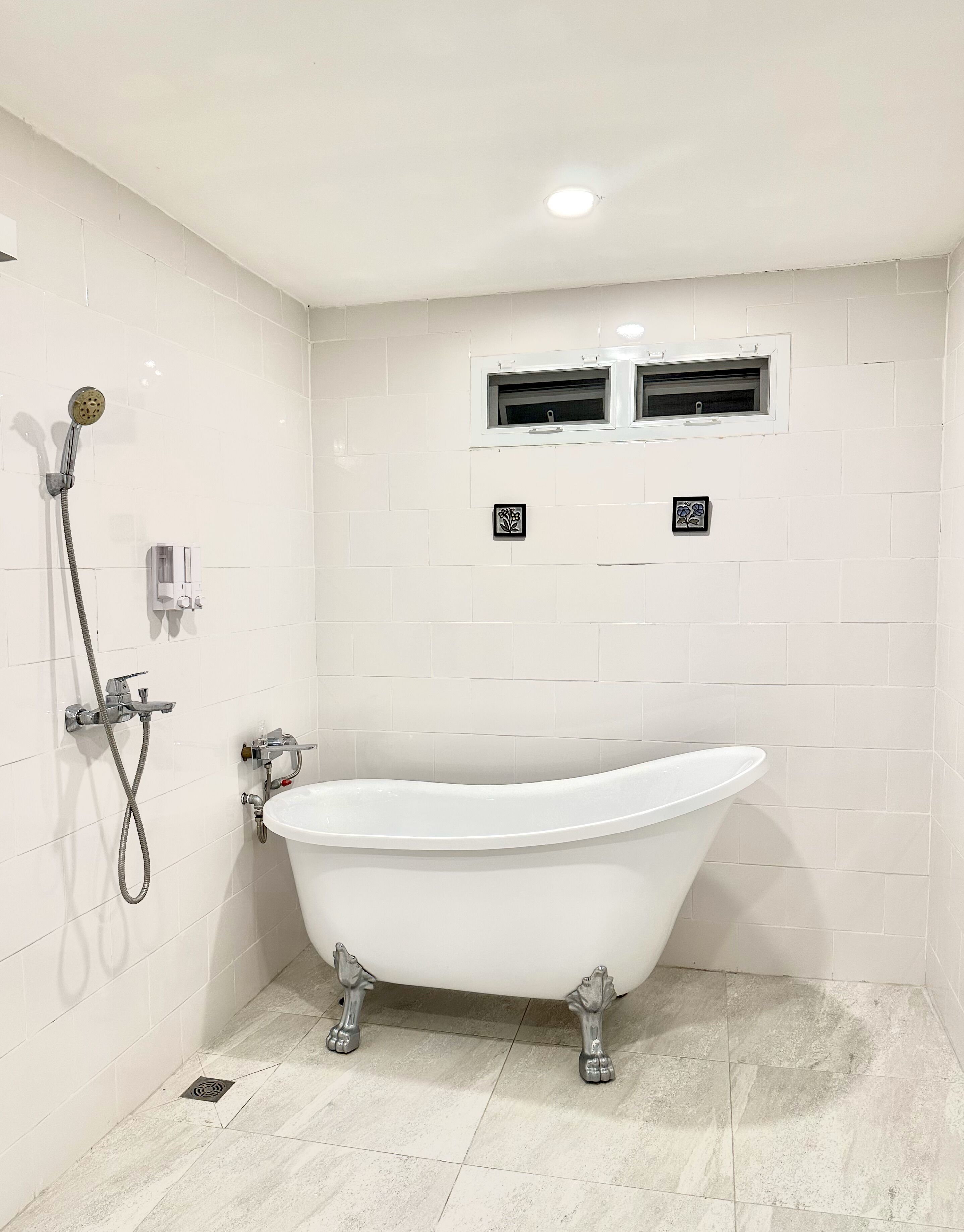 A bathroom with a freestanding bathtub, a showerhead, and a window with ventilation.
