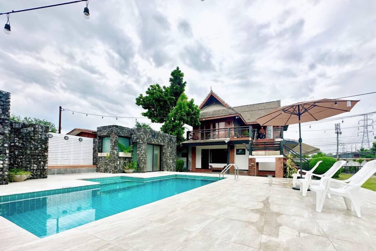 A modern house with a swimming pool, stone walls, and a large patio area with lounge chairs.