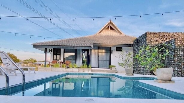 Una casa moderna con piscina, area relax esterna e un muro in pietra.