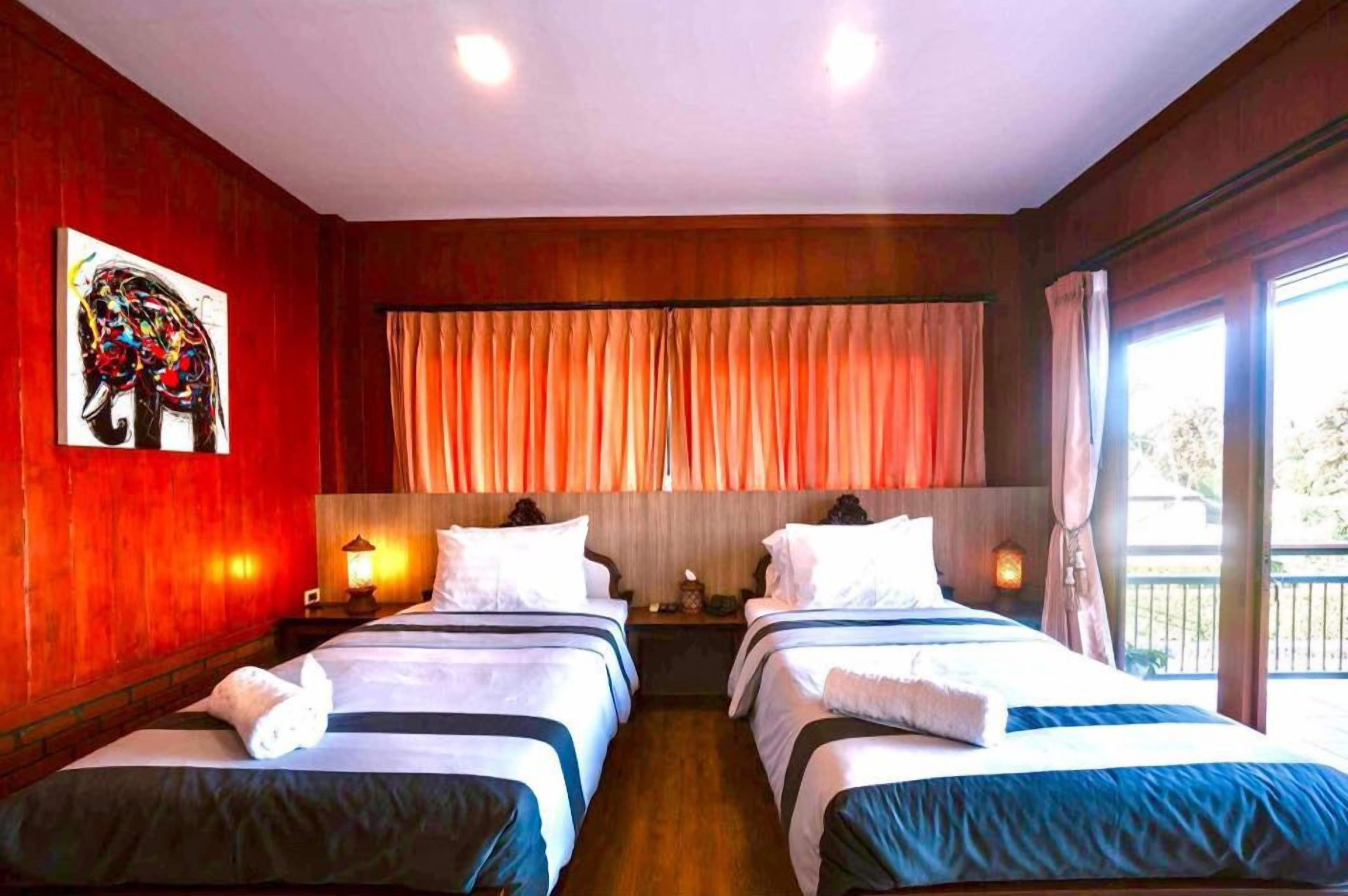 A hotel room with two beds, a large window with curtains, a painting on the wall, and a balcony.