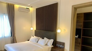 A modern bedroom with a large bed, bedside tables, a wall-mounted air conditioner, and a built-in wardrobe. - Polo Grand Hotel (Maiduguri)