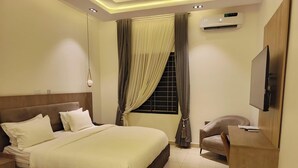 A hotel room with a large bed, a TV, a desk, and an air conditioning unit. - Polo Grand Hotel (Maiduguri)