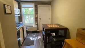 A compact kitchen with a dining table and chairs, a refrigerator, and a microwave. - Central Farmhouse-Style Micro Apartment (Lethbridge)