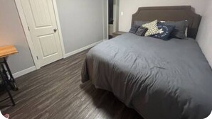A bedroom with a bed, a door, and a small table. - Central Farmhouse-Style Micro Apartment (Lethbridge)