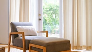 Une pièce avec une grande fenêtre, un canapé gris avec un coussin et une chaise en bois.