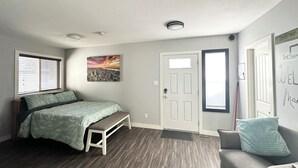 Un dormitorio con cama, banco, obra de arte urbana, una puerta y una silla.