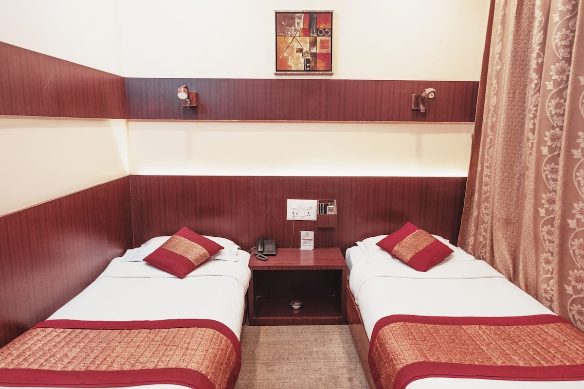 Une chambre d’hôtel avec deux lits, une petite table avec un téléphone, une prise électrique et un tableau.