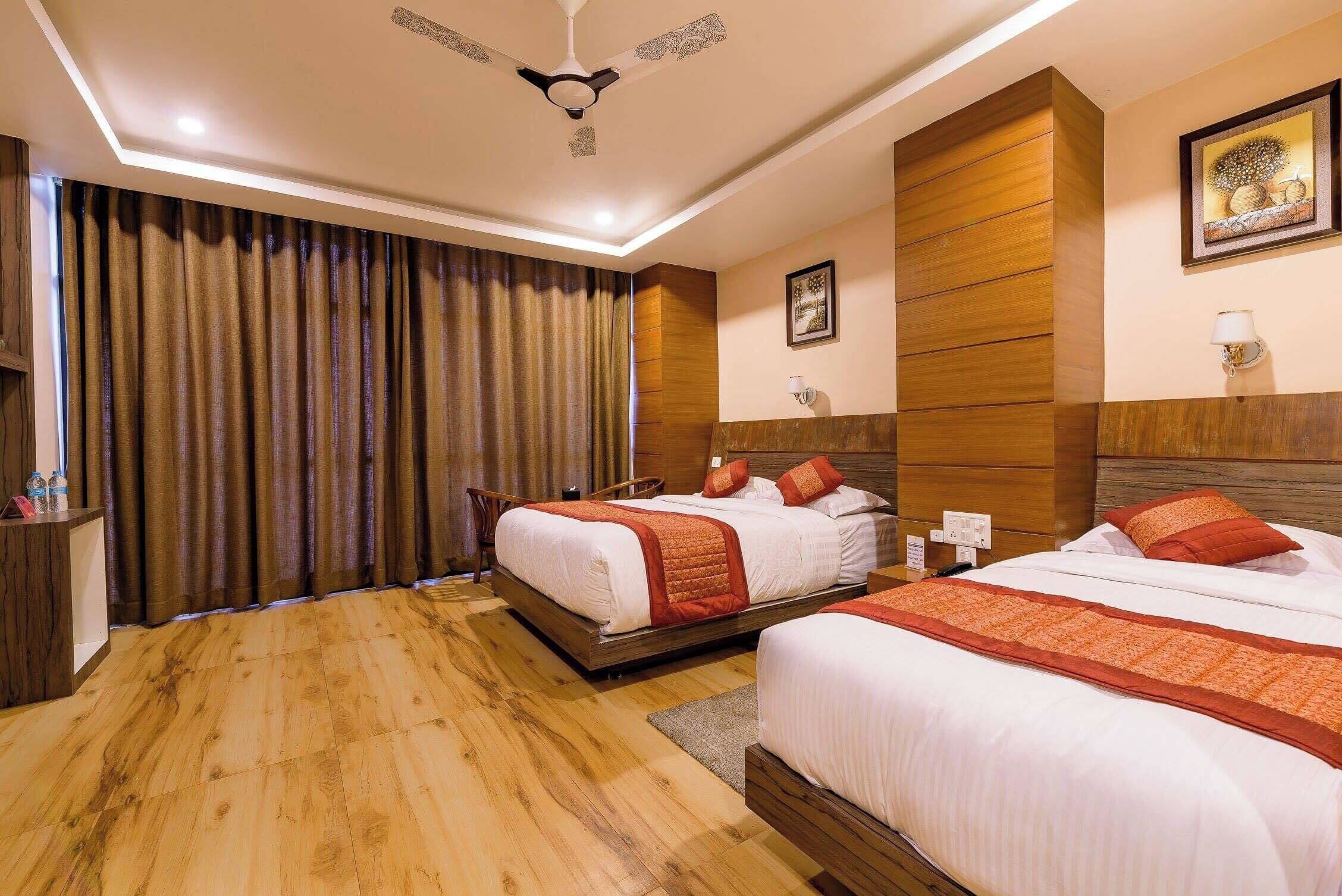 Habitación de hotel con dos camas, piso de madera, ventilador de techo y un ventanal grande con cortinas.