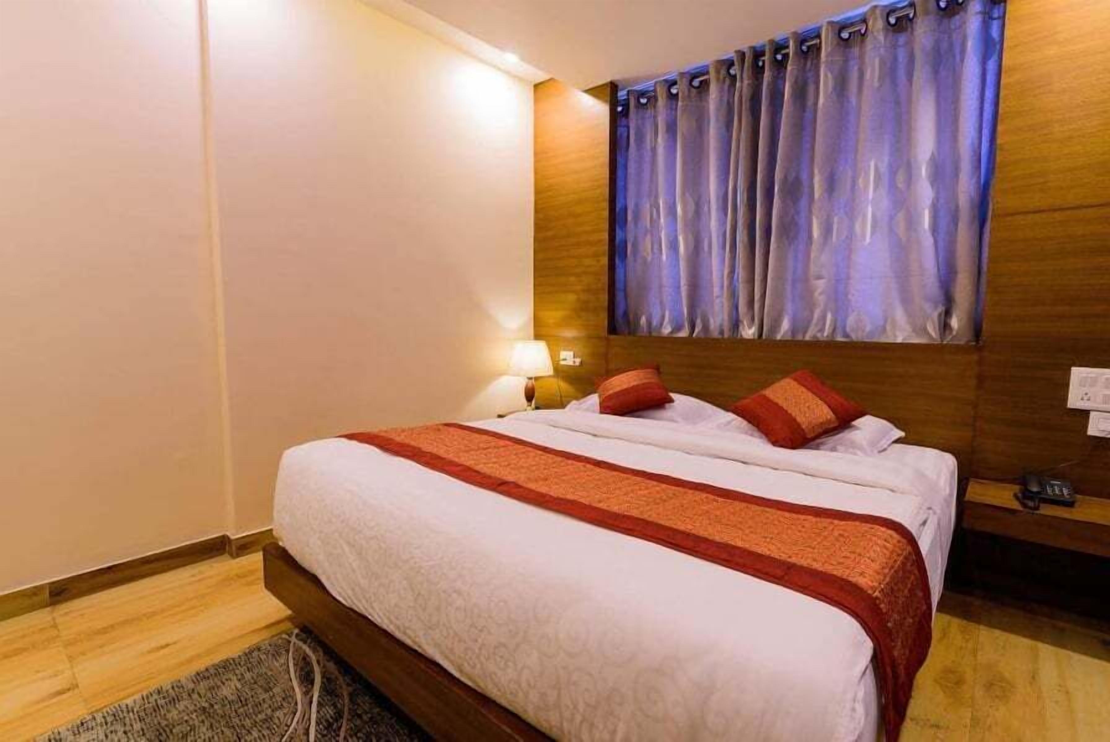 A hotel room with a large bed, wooden headboard, and a curtain with a blue and white pattern.