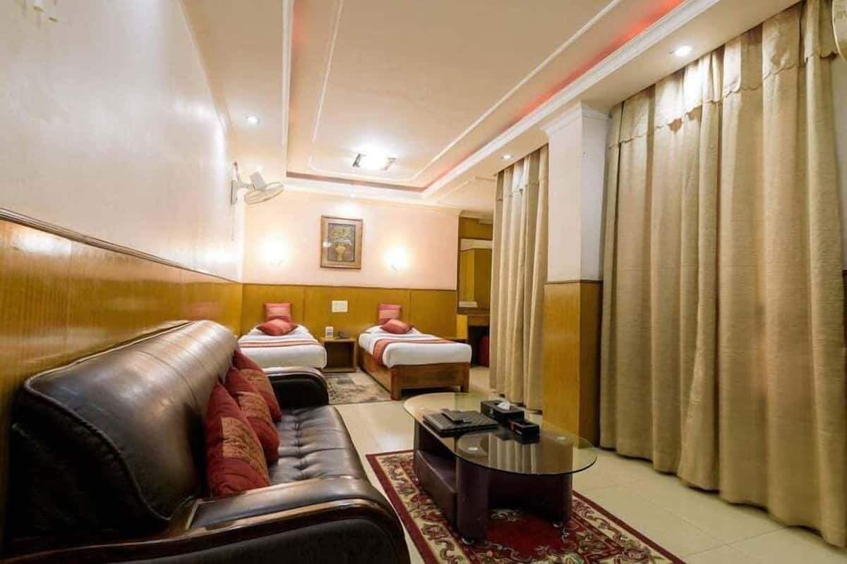 Une chambre d’hôtel avec un canapé en cuir, deux lits simples, une petite table et une grande fenêtre avec des rideaux.