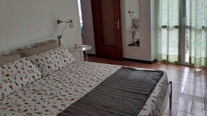 A bedroom with a bed, a bedside table, a lamp, a door, and a window with curtains. - CasaRina Poggi - 360° Panoramic Terrace from the Mountains to the Sea and Relaxation in Imperia (Poggi)