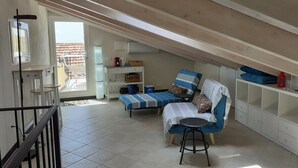 A cozy attic bedroom with a bed, a chair, a small table, and a wardrobe. A window provides natural light, and a balcony is visible outside. - CasaRina Poggi - 360° Panoramic Terrace from the Mountains to the Sea and Relaxation in Imperia (Poggi)