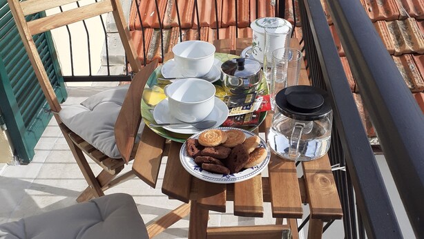 A wooden table with a green tray, two white cups, a teapot, a glass, and cookies on a balcony with terracotta tiles. - CasaRina Poggi - 360° Panoramic Terrace from the Mountains to the Sea and Relaxation in Imperia (Poggi)