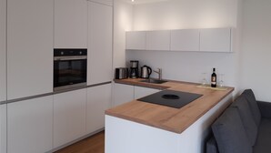 A modern kitchen with white cabinets, a built-in oven, a coffee maker, and a wine bottle on the counter. - Apartment Panorama Walensee (Glarus Nord)