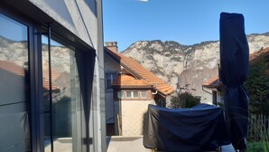 A modern building with large glass doors, a covered outdoor seating area, and a view of a mountainous landscape. - Apartment Panorama Walensee (Glarus Nord)