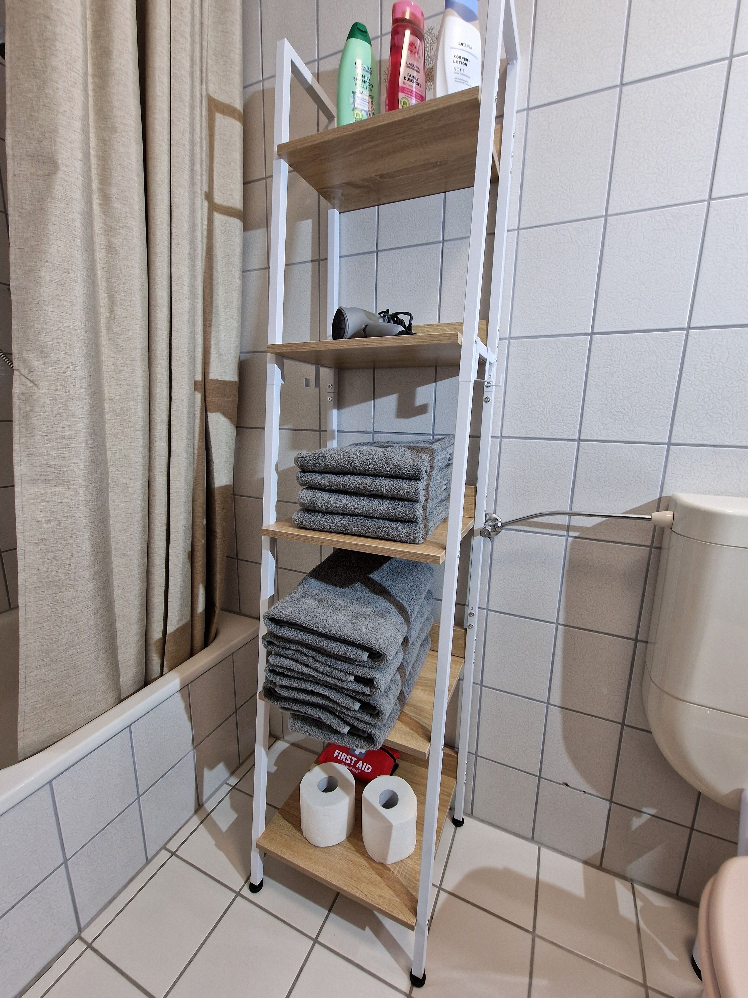 Een badkamer met een metalen plank waarop toiletartikelen, handdoeken en toiletpapier liggen.