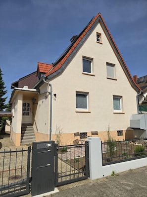 Une maison à deux étages, avec un toit en pente, une porte d’entrée et un petit porche.