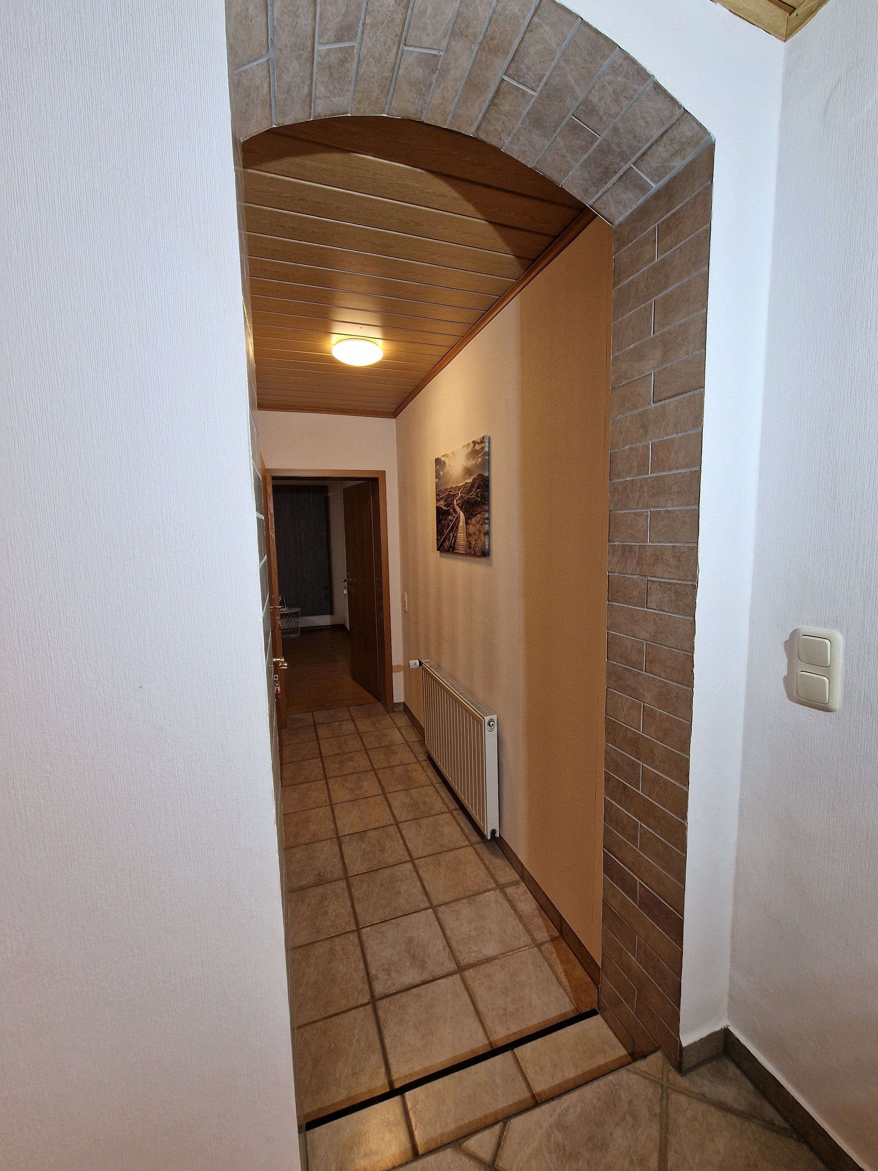 Een gang met een betegelde vloer, een bakstenen muur en een plafond met houten balken.