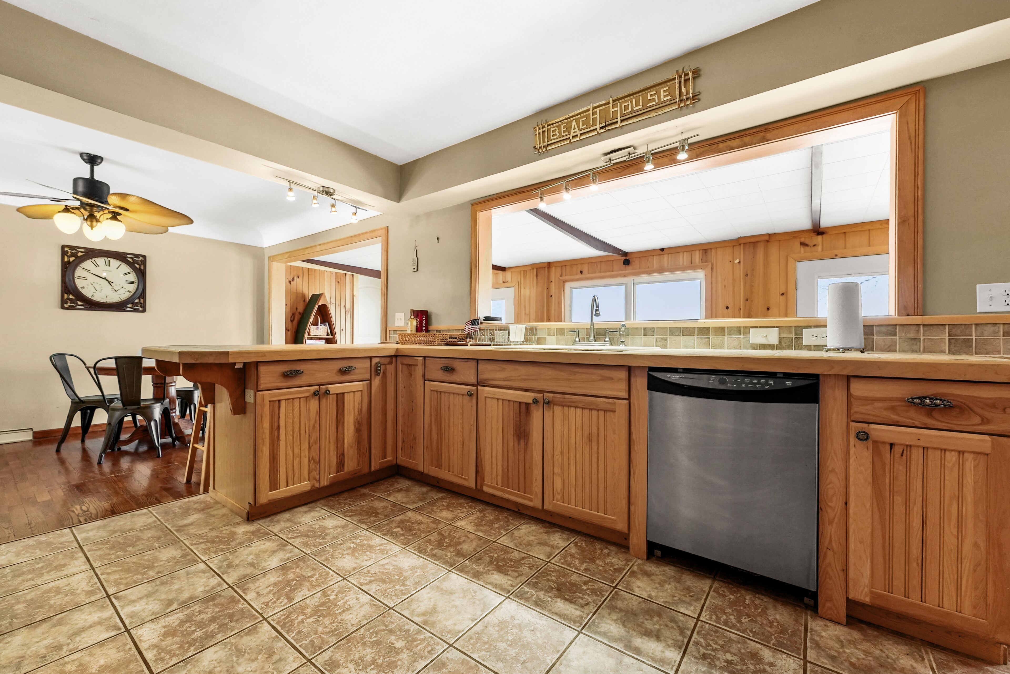 A kitchen with wooden cabinets, a dishwasher, a ceiling fan, and a clock on the wall.