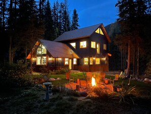 A two-story cabin with a metal roof, large windows, and a fire pit in the yard. - River Run Lodge - Your Tranquil Retreat 20 minutes from Glacier National Park (Essex)