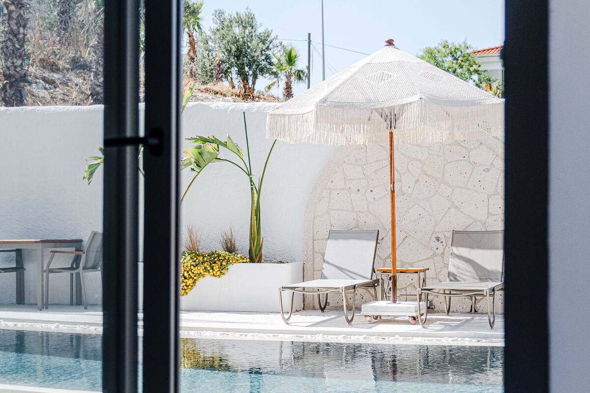 Ein moderner Poolbereich mit Glaswänden, einer Steinwand und einer Sitzecke mit zwei Liegestühlen und einem Tisch.