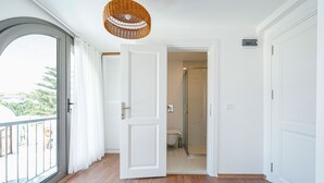 Quarto com uma grande janela, porta de acesso a um banheiro e luminária de palha no teto.