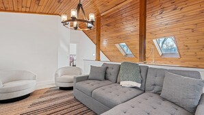 Un cuarto estilo loft con techo de madera, un sofá seccional gris, un sillón redondo y una alfombra estampada.