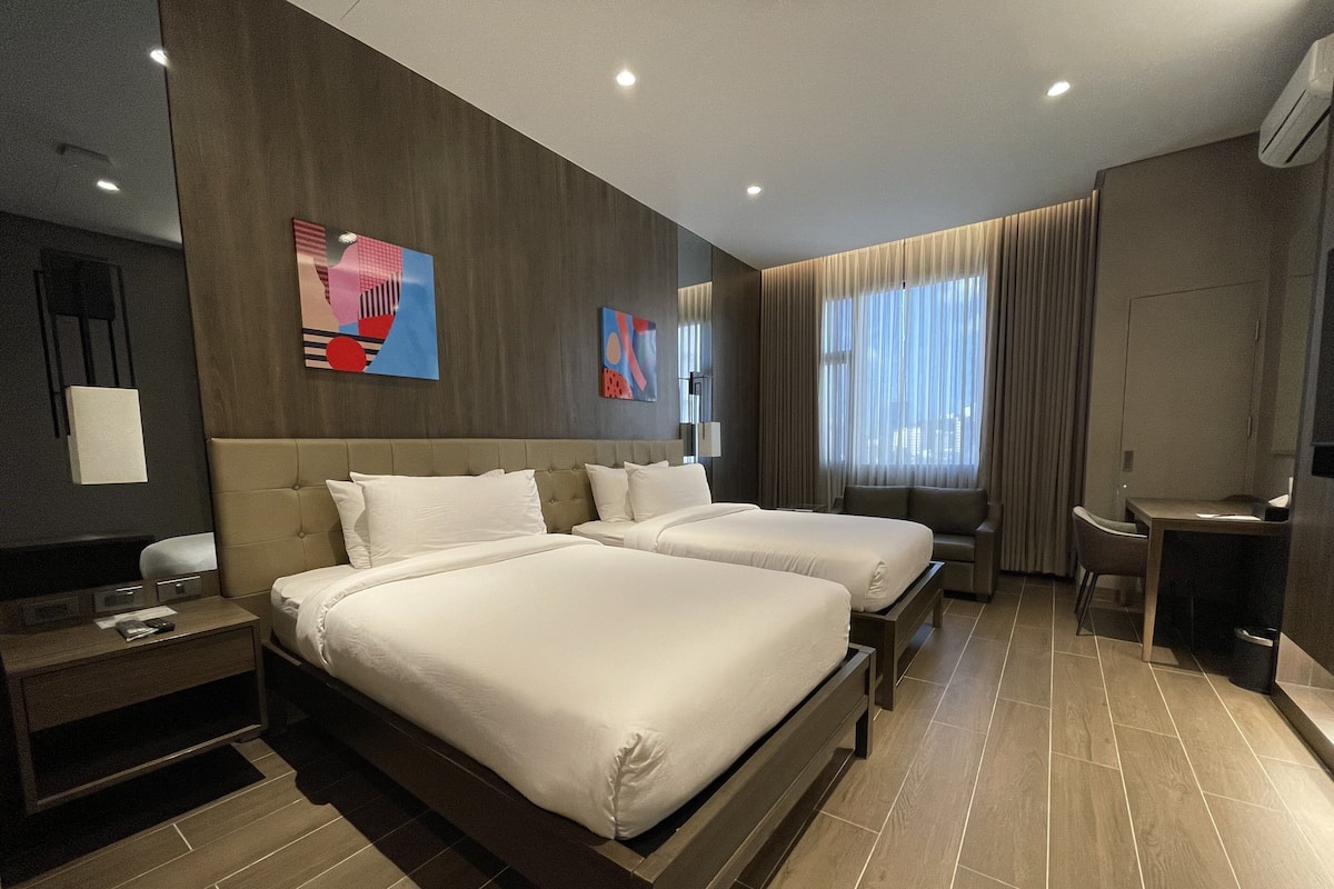 A modern hotel room with two beds, a desk, and a chair.