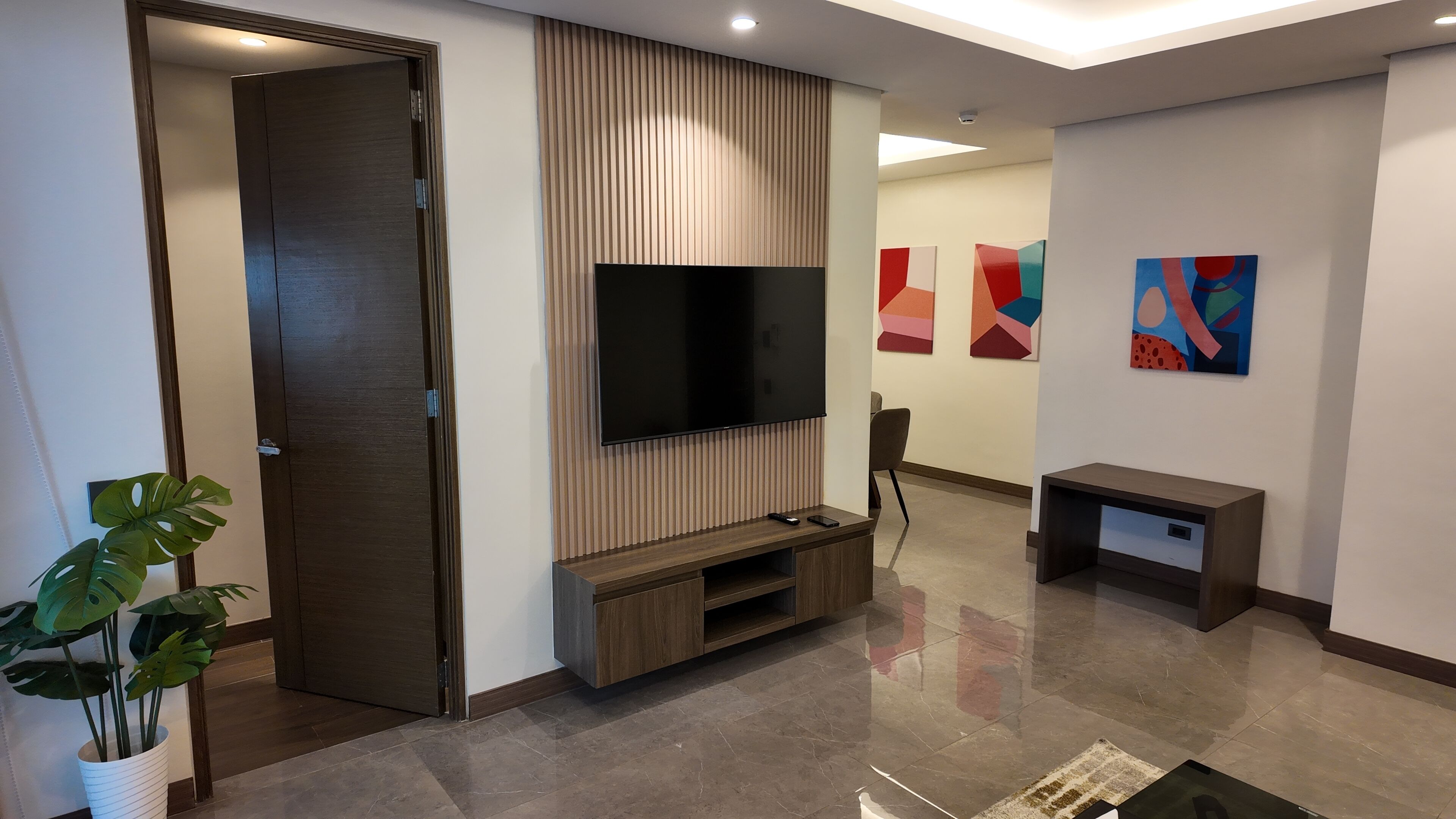 Un salon moderne doté d’un téléviseur à écran plat, d’un mur recouvert de panneaux en bois et d’œuvres d’art abstraites.