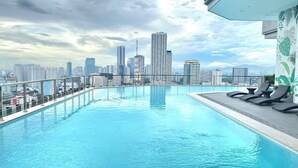 Una piscina en la azotea con vistas al horizonte urbano, sillas de descanso y un diseño arquitectónico moderno.