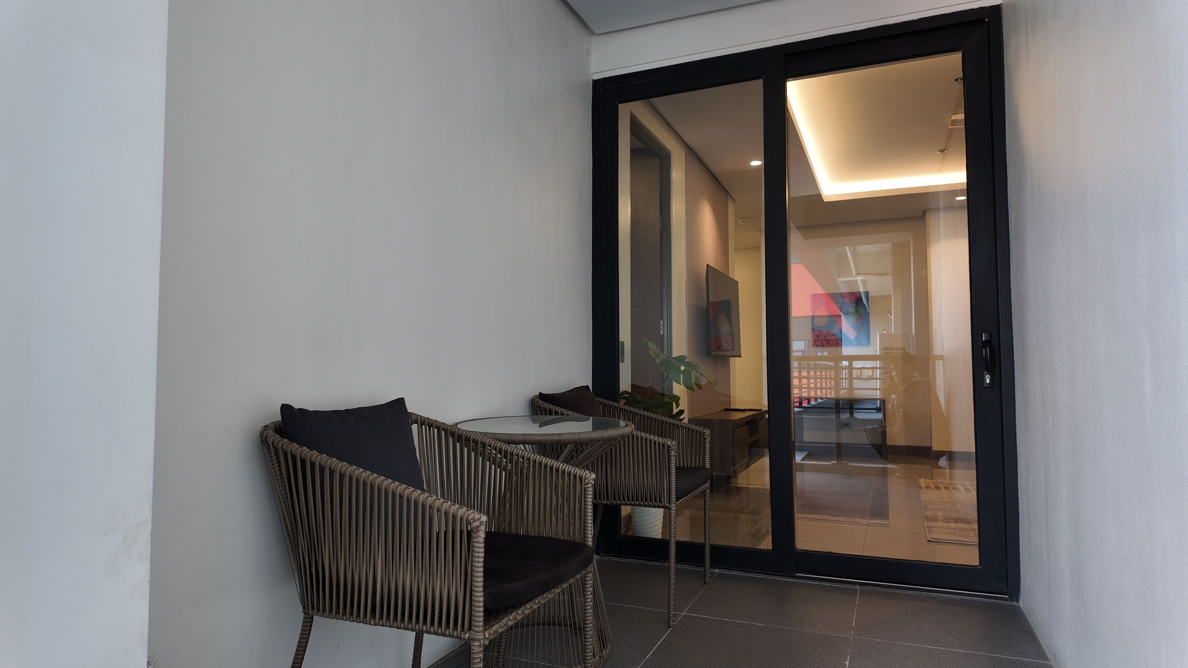 Una habitación con una puerta de cristal que da a un balcón, amueblada con sillas de mimbre y una mesa.
