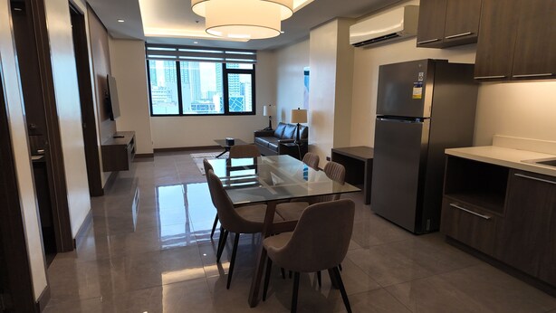 Una cocina moderna con una mesa de comedor de vidrio, armarios oscuros y un refrigerador.