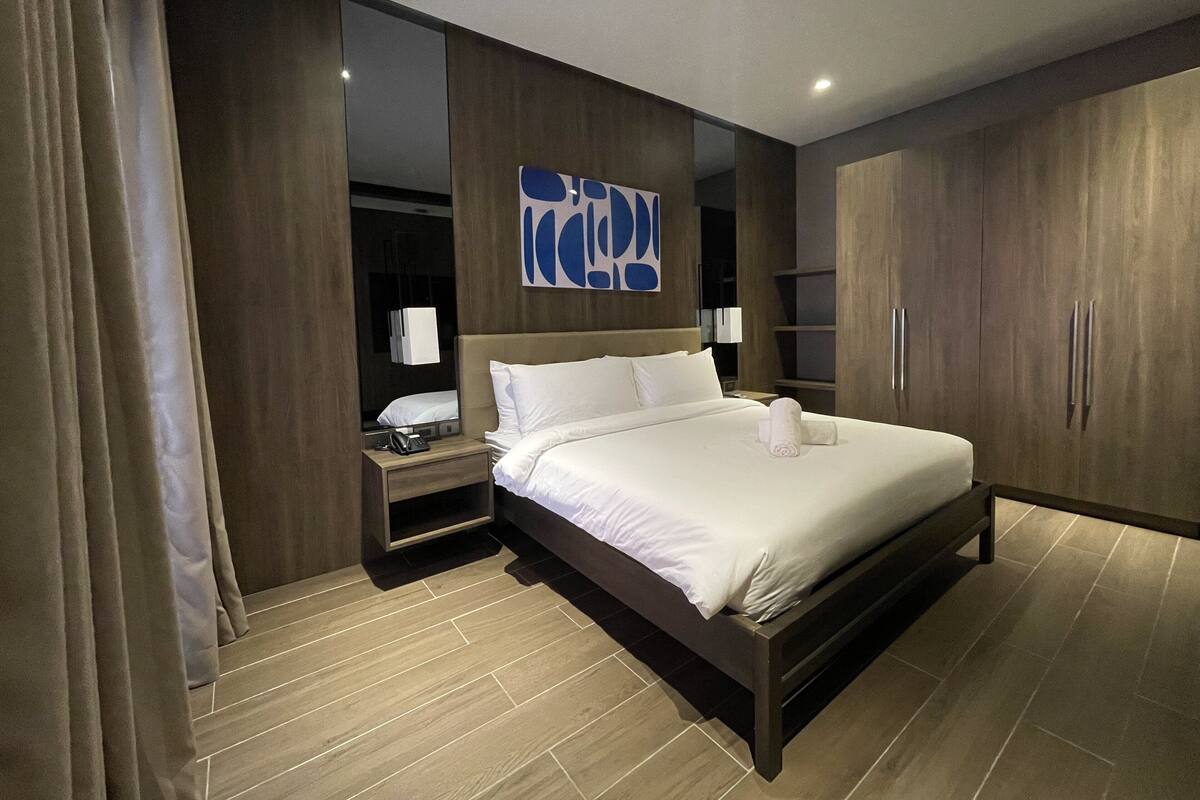 A modern hotel room with a large bed, wooden wardrobe, and a mirror.
