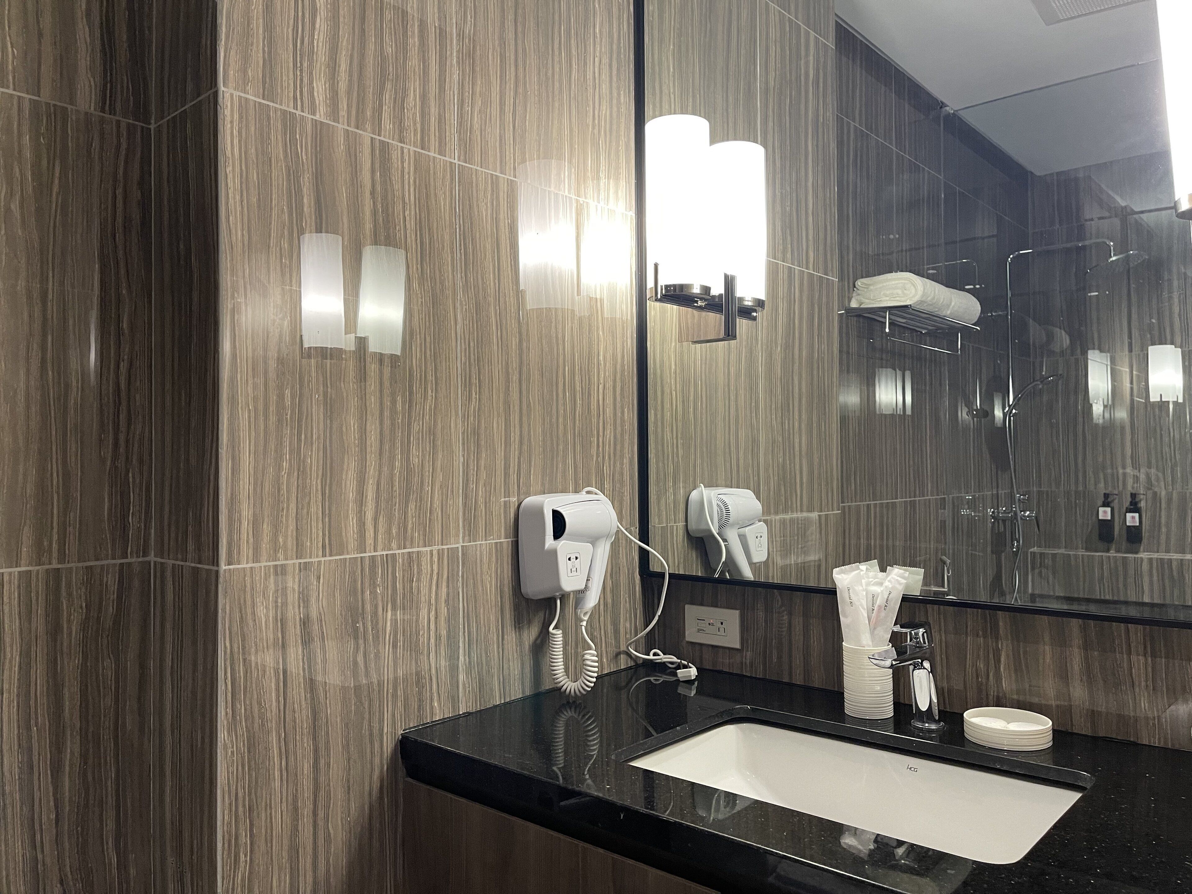 A modern bathroom with a black countertop, a sink, a mirror, a hairdryer, and a towel dispenser.