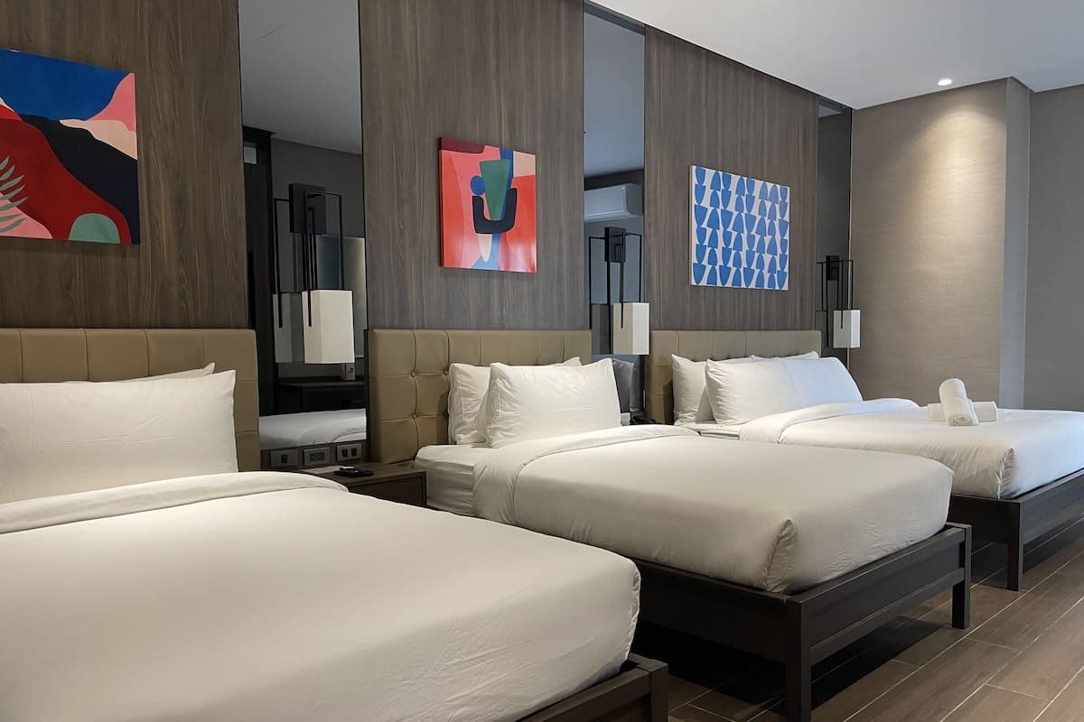 A hotel room with three beds, a large window, and modern decor.